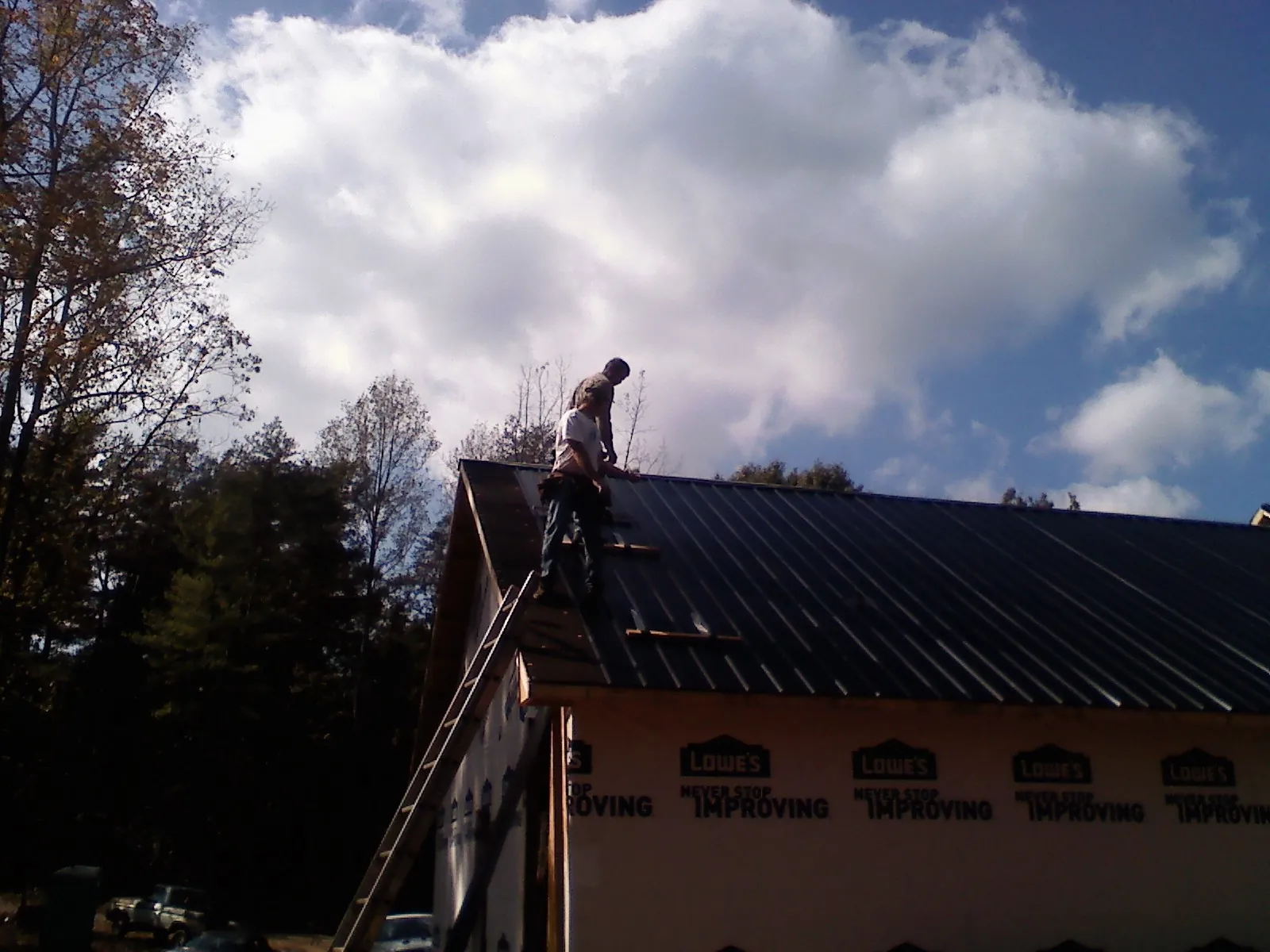 Roofer fastening dark metal panels high against a cloudy sky, from a Roof Inspection job in Williamsfield